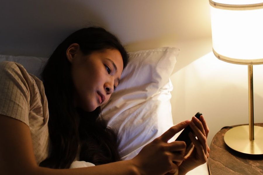 불 끈 침실에서 스탠드 불빛에 기대 휴대폰 화면을 보고 있는 사람